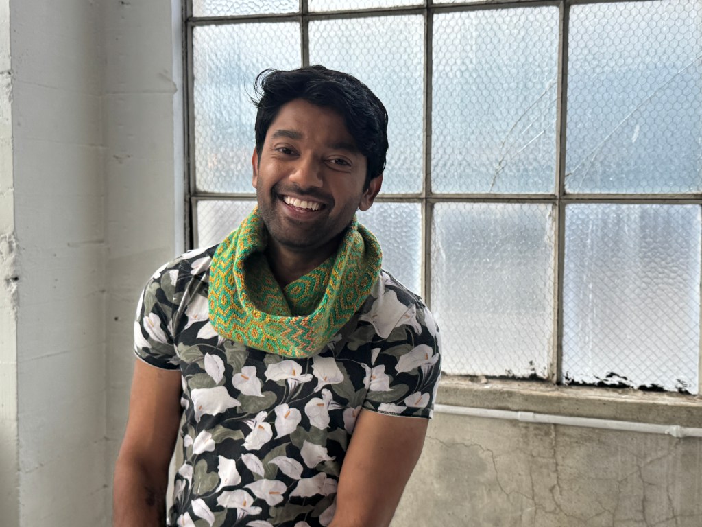 Smiling man in a calla lily print T-shirt, wearing the green and orange-yellow Kaleidocowl