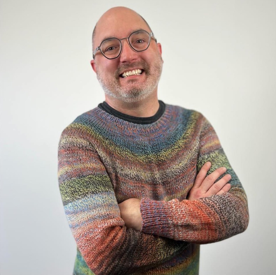 Kyle Kunnecke smiling with arms crossed, wearing a hand-knit striped sweater